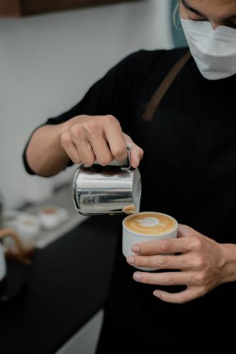 a woman in a mask is making a cup of coffee at CERIA HOTEL at Alun Alun Yogyakarta in Yogyakarta