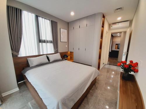 a bedroom with a large white bed and some flowers at TSQ STAY Hotel Apartment in Hanoi