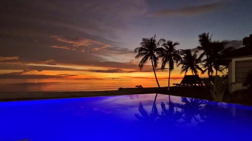 a sunset over the ocean with a pool and palm trees at Blue Joys MSR in Siquijor