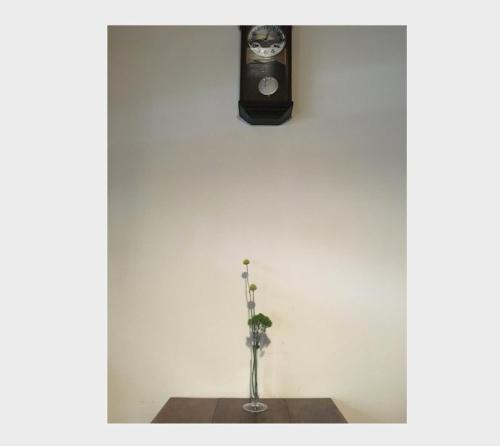 a vase on a table with a clock on a wall at あずきや in Kyoto