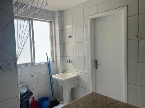 a white bathroom with a sink and a window at Apartamento Guarapari Frente para o Mar in Guarapari