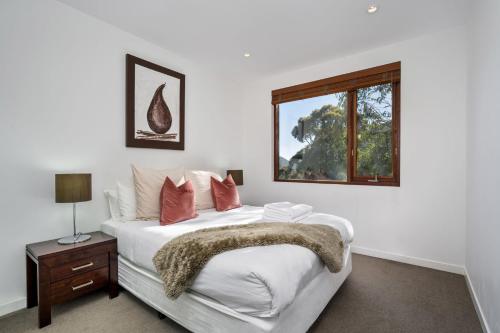 Dormitorio blanco con cama y ventana en Elevation 2 bedroom with guest room gas fire and mountain views, en Thredbo