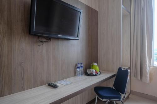 a room with a television on a wall with a chair at Sans Hotel Lynt Makassar in Makassar