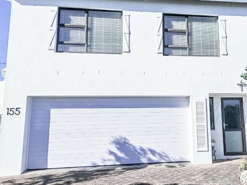 a white house with a garage door and two windows at Struispaleis in Struisbaai