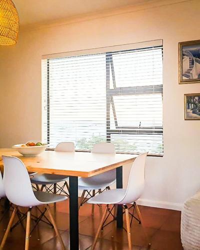 a dining room table with white chairs and a window at Struispaleis in Struisbaai