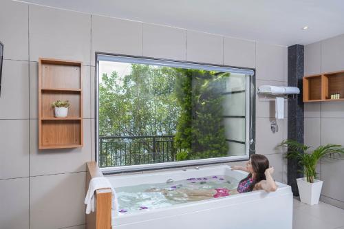 Sprise Munnar Resort and Spa في مونار: فتاة صغيرة كانت تجلس في حوض الاستحمام مع نافذة