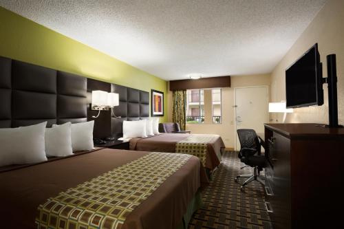a hotel room with two beds and a flat screen tv at Days Inn by Wyndham Dallas Irving in Irving