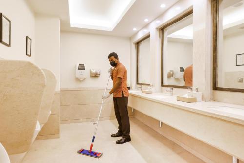 a man standing in a bathroom with a mop at Lemon Tree Premier, Ulsoor Lake, Bengaluru in Bengaluru