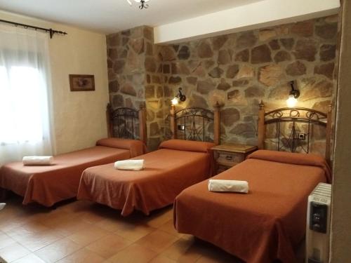 Habitación de hotel con 2 camas y pared de piedra. en Hotel Villa de Berzocana en Berzocana
