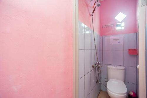 a bathroom with a toilet and a pink wall at RedDoorz near Simpang Bandara SMB II in Palembang