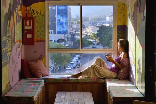 a woman sitting on a window sill looking out the window at Tiberias Hostel in Tiberias
