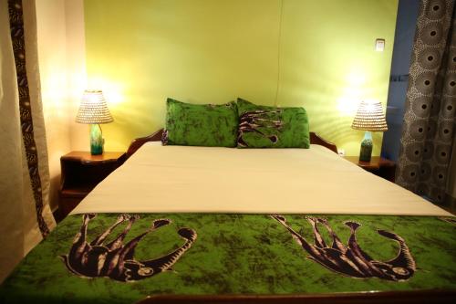a bedroom with a bed with green sheets and two lamps at Tea House BNB in Kigali
