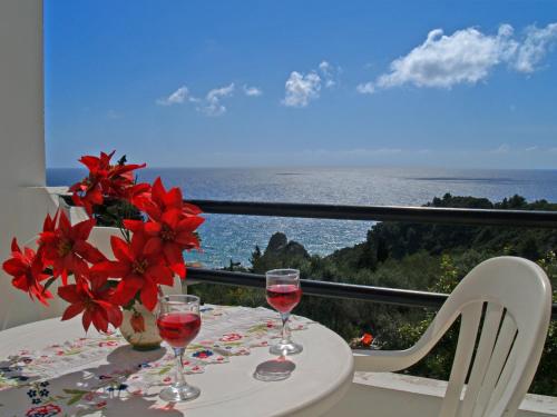 a table with two glasses of wine and flowers on it at Studio Apartment with adult and childrens pool and sea view - Pelekas Beach in Pelekas