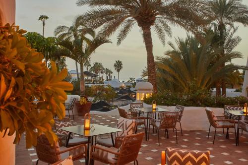 a patio with tables and chairs and palm trees at Dreams Jardin Tropical Resort & Spa in Adeje