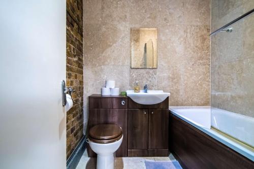 La salle de bains est pourvue de toilettes, d'un lavabo et d'une baignoire. dans l'établissement Livestay-Fabulous Three Bed Warehouse Conversion Apartment, à Londres