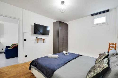 une chambre blanche avec un lit et une télévision à écran plat dans l'établissement Grand Appartement aux Portes de Paris, à Aubervilliers