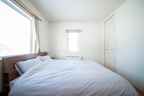 a bedroom with a white bed and a window at The Sanfurano in Kami-furano
