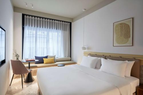 Un dormitorio con una gran cama blanca y una ventana en The Social Athens Hotel, a member of Radisson Individuals, en Atenas