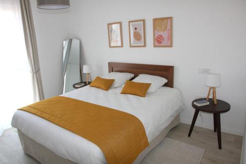 una camera da letto con un grande letto con lenzuola bianche e cuscini arancioni di DOMITYS LES SALINES a Cherbourg en Cotentin