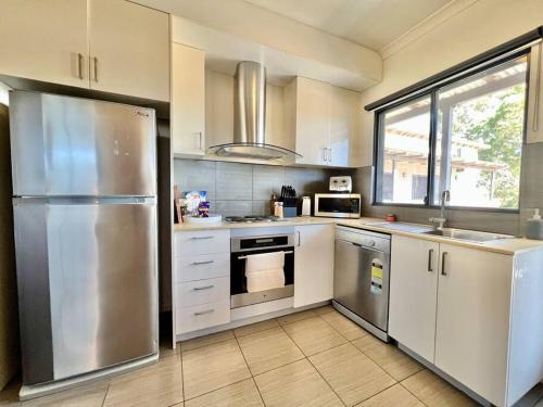 cocina con armarios blancos y nevera de acero inoxidable en Stylish Self-contained Apartment, en South Hedland