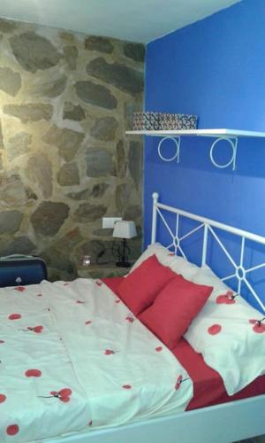 a bedroom with a bed with red pillows and a stone wall at Apartamento casco antiguo Vejer in Vejer de la Frontera
