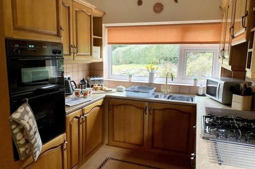 a kitchen with wooden cabinets and a sink and a window at Little Acre, a spacious hidden gem with hot tub in Kington