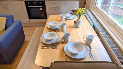 a wooden table with plates and a vase of flowers on it at Leamington Spa Warwick Place Apartments in Leamington Spa
