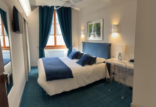 a bedroom with a bed with blue pillows and a desk at Logis Hôtel des Messageries in Arbois