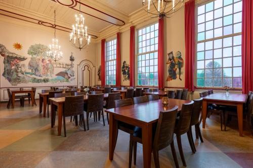 a dining room with tables and chairs and windows at Stayokay Hostel Heemskerk in Heemskerk