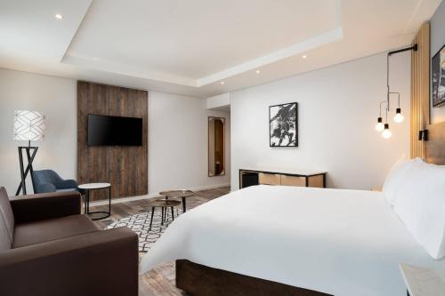 a bedroom with a large white bed and a living room at Protea Hotel by Marriott Johannesburg Wanderers in Johannesburg