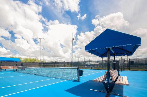 a tennis court with two benches and an umbrella at The Santa Maria, a Luxury Collection Hotel & Golf Resort, Panama City in Panama City