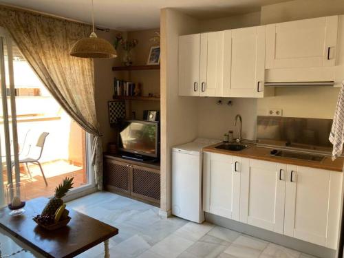 Il comprend une cuisine avec des placards blancs, une table et une télévision. dans l'établissement Coqueto y acogedor apartamento con piscina, à Roquetas de Mar