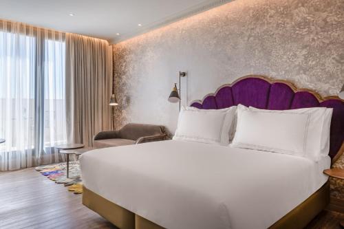 - une chambre avec un grand lit blanc et une tête de lit violette dans l'établissement Querencia de Sevilla, Autograph Collection, à Séville