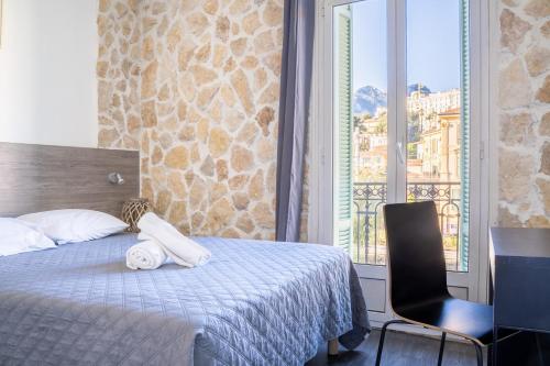 una camera con un letto e una sedia e una finestra di Hotel De Belgique à Menton a Mentone