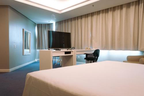 a hotel room with a bed and a desk with a television at Master Porto Alegre Hotel - Av Carlos Gomes, Próximo ao Consulado Americano in Porto Alegre
