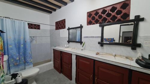 a bathroom with two sinks and a toilet and a mirror at Charming 2-Bed Cottage in Bodo a fishing village in Funzi
