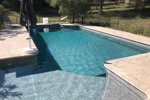 a swimming pool with an umbrella in a yard at Beautiful house in the heart of its pine forest - private pool in Les Taillades