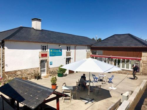 a person sitting under an umbrella in front of a building at Albergue Ponte Ferreira CAMINO PRIMITIVO Lugo - Ferreira in Lugo