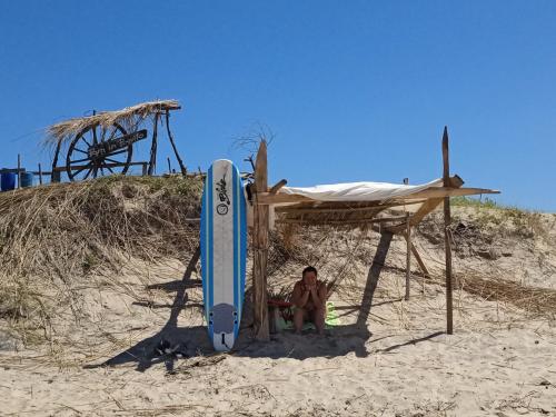 un hombre sentado en una silla junto a una tabla de surf en la playa en Para un poquito relax, en Barra de Valizas