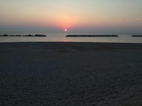 a sunset on the beach with rocks in the water at Camping La Pineta in Porto Recanati