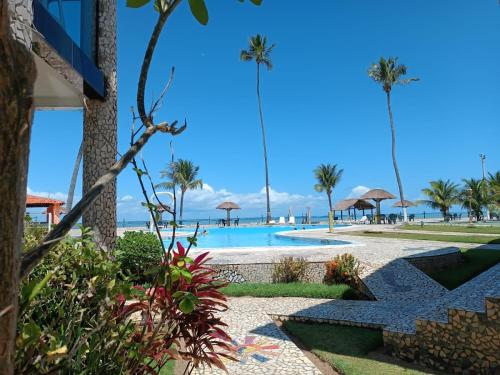 uma piscina com palmeiras e uma praia em Village Galés de Maragogi em Maragogi