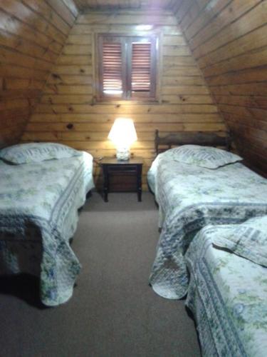 a room with two beds and a lamp on a table at Chalé Lady in Campos do Jordão
