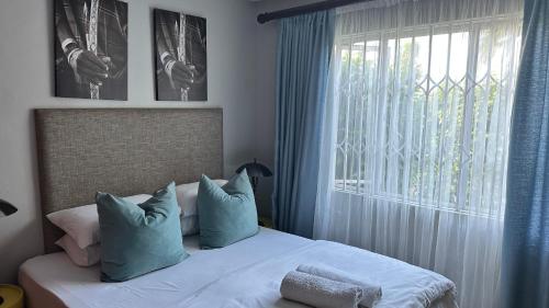 a bedroom with a bed with blue pillows and a window at KADESE Holiday North Beach Durban in Durban