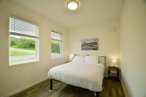 a white bedroom with a bed and two windows at Rockfish Retreat at Kachemak Bay Kabins in Homer
