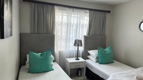 a bedroom with two beds with green pillows and a window at KADESE Holiday North Beach Durban in Durban