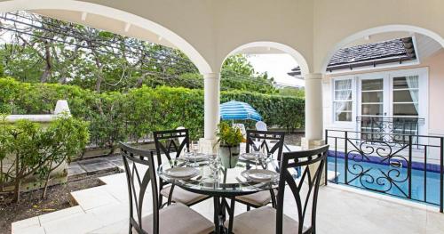 un patio con mesa, sillas y piscina en The Falls Villa 1 by Barbados Sothebys International Realty en Saint James
