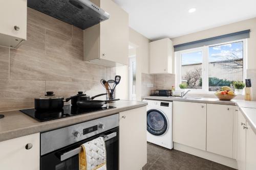 cocina con armarios blancos, lavadora y secadora en Cosy 2 Bedroom Ground Floor Apartment with Garden - Coventry, en Coventry