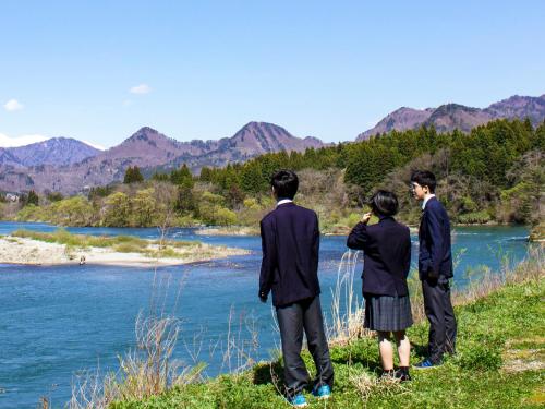 three people standing on a hill looking at a river at 津川温泉 清川高原保養センター in Aga