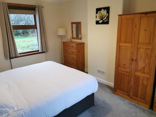 BanavieにあるLaxdale Cottageの白いベッドと木製キャビネット付きのベッドルーム1室が備わります。
