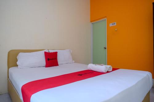 a white bed with a red pillow on top of it at RedDoorz @ Jalan Pramuka Manado in Manado